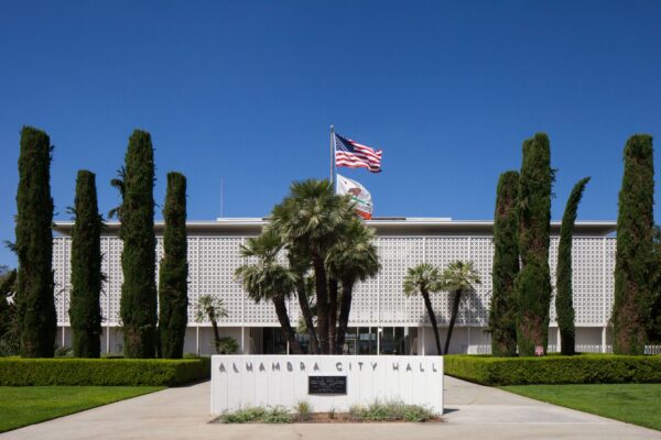 The front view of Alhambra's City Hall, with a sign that says "Alhambra City Hall," and the American and California state flags waving in the air.